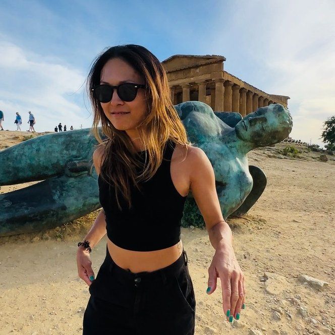 Woman in sunglasses walking near the Acropolis with a reclining statue in the foreground