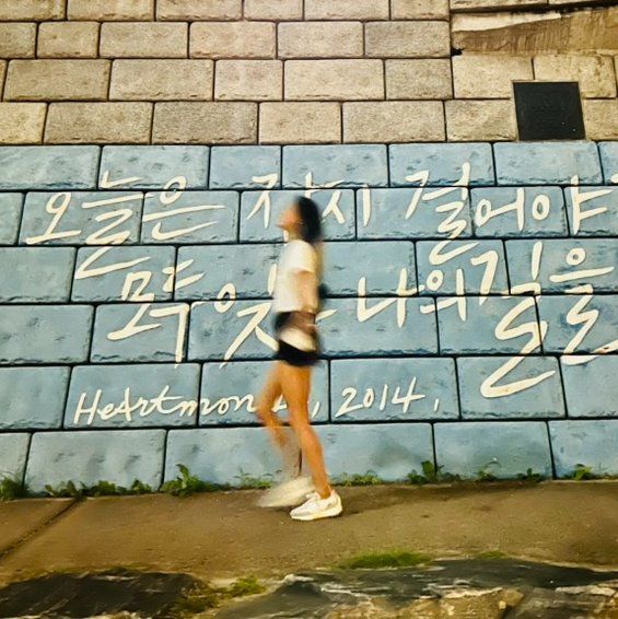 Person walking past a stone wall with Korean writing graffiti in warm evening light